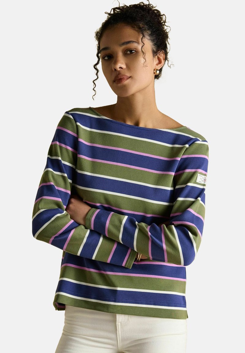 Kortsukli naise juuksed on lokkis, ta kannab pikki varrukatega särke, millel on horisontaalsed laevakujulised, oliivrohelised, roosad ja valged triibud, käed on ristis ja jalas on heledad püksid.