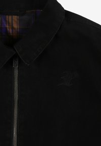 Czarna kurtka dżinsowa z zamkiem błyskawicznym, kołnierzykiem i wytłoczonym logo na piersi. Wnętrze wykończone jest wydrukiem w kratę.