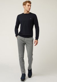 Maglione blu navy a collo rotondo e pantaloni grigio chiaro. Il maglione è realizzato in un tessuto liscio con polsini a coste. Le scarpe da ginnastica sono scure con accenti blu.