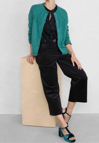 Turkusowy kardigan z teksturowanymi ramionami, czarny top z wzorem, czarne sztruksowe spodnie o szerokich nogawkach oraz turkusowe sandały na klockowym obcasie.