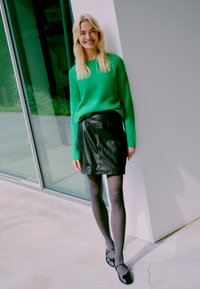 Žalias pūkuotas megztinis, juoda odinė mini sijonas, juodos pėdkelnės ir juodi bateliai. Lygi tekstūra, prigludęs dizainas ir kasdienis stilius.