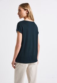 Mørk navy t-shirt med rullede ærmer, lavet af blødt stof. Den har en afslappet pasform og en rund kant, parret med lyse beige bukser.