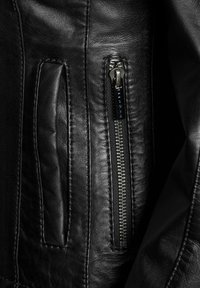 Crna kožna jakna s patentnim zatvaračem i glatkom teksturom, s istaknutim šavovima i elegantnim detaljima patentnog zatvarača.