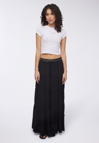 T-shirt bianco corto con design a farfalla, abbinato a una gonna maxi nera a strati con vita regolabile e una finitura testurizzata.