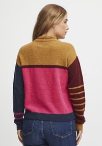 Pull en laine mélangée avec des rayures en blocs dans des teintes de moutarde, bordeaux, rose et marine. Texture tricotée, col et poignets côtelés, avec des manches à accent rayées.