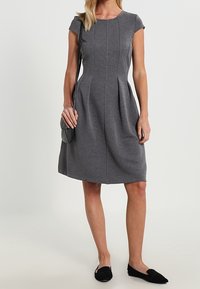 Grå klänning med kort ärm som har en figursydd livdel med veck, slät textur och midilengd. Matcher med svarta flator och en liten väska.