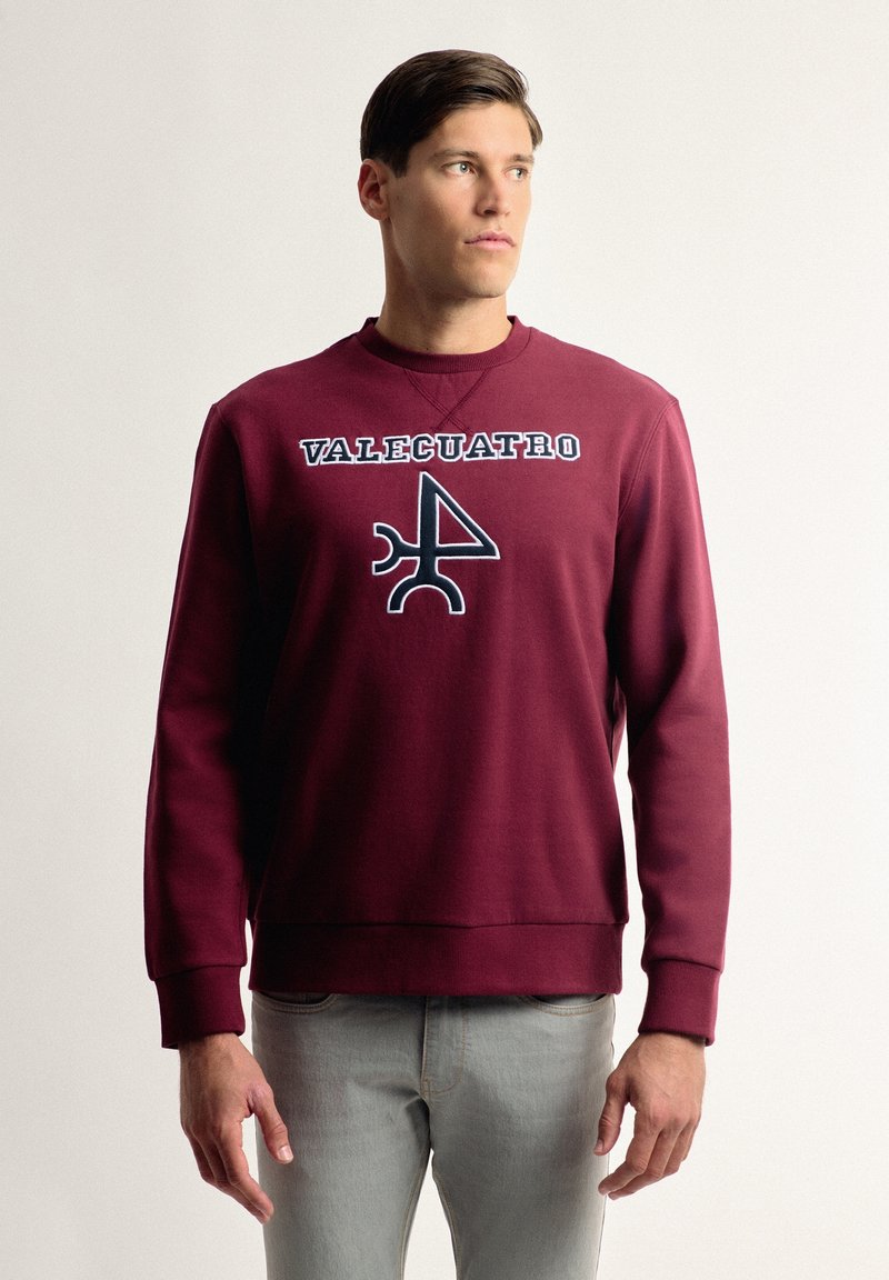 Sudadera color burdeos con cuello redondo y puños de canalé, con un logo gráfico "VALCUATRO" y un diseño abstracto en negro.