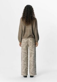 Suéter de punto marrón con mangas globo, combinado con pantalones de pierna ancha que presentan un patrón de rayas de cebra en beige y gris. Calzado negro.