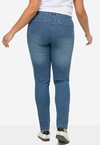 Úzke modré džínsy vyrobené z denimu, s stredne vysokým pásom, dizajnom s piatimi vreckami a jemným vyblednutím, skombinované s bielymi a čiernymi teniskami.