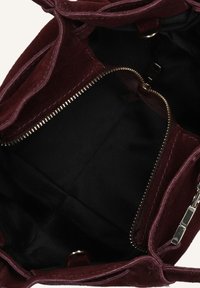 Bordeaux suède tas met een zwarte stoffen binnenkant, voorzien van een ritszak en meerdere compartimenten voor ordelijkheid.