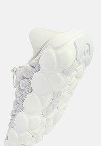 Vit strukturerad sneaker-sula med bubbelliknande dämpning och ovandel i stickad tyg, sedd från snett under- och sidan.