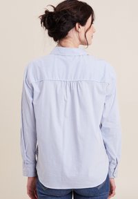 Camicia a righe azzurro chiaro e bianca con maniche lunghe, polsini con bottoni e dettaglio sulla spalla. Tessuto morbido con vestibilità rilassata e orlo curvo.