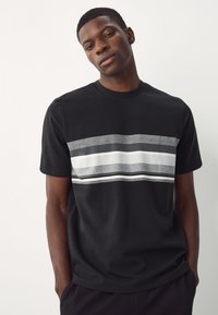 T-shirt nera in cotone con strisce orizzontali grigie e bianche sul petto, maniche corte e scollo rotondo.