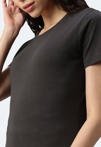 T-shirt nera in cotone con maniche corte e un semplice collo a giro. Il tessuto ha una texture liscia e una silhouette aderente.