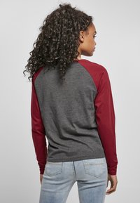 Langarmshirt mit grauem Körper und kastanienbraunen Raglansleeves. Weiches Baumwollmischmaterial, lässige Passform mit abgerundetem Saum.