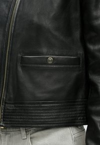 Μαύρο δερμάτινο μπουφάν με φερμουάρ, υφή επιφάνειας, ριμπ λεπτομέρεια στο τελείωμα και μικρό μεταλλικό λογότυπο στην τσέπη στο στήθος.