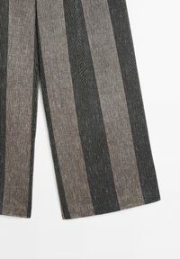 Pantalon large gris et noir avec un motif à rayures verticales sur fond blanc.