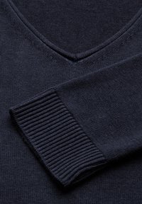 Mörkblå stickad tröja med V-ringad design, ribbade ärmslut och slät textur, med en närbild av halsringningen och ärmen.