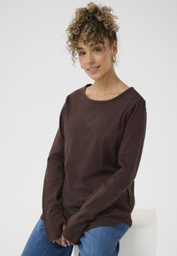 Brun langærmet top lavet af blødt bomuld med en bred halsudskæring. Bæres med blå jeans, har løse ærmer og en afslappet pasform.