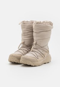 Botas acolchadas de color beige, aisladas, con una parte superior acolchada, parte superior ajustable con cordón y suela de goma resistente con picos de tracción.