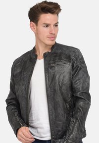 Chaqueta de cuero negra con detalles texturizados, cierre delantero con cremallera y bolsillos laterales. Presenta un diseño minimalista y una silueta ajustada.