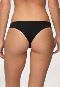 Slip bikini neri con una texture liscia, design a vita bassa e copertura minima. Le cuciture sono pulite, senza hardware o motivi visibili.