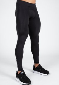 Black active leggings with a smooth texture, high waistband, and fitted design. Pair of black athletic shoes completes the outfit.