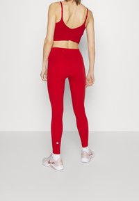 Červený sportovní crop top s ramínky a odpovídající červené legíny. Legíny mají bezešvý design a texturované prvky.