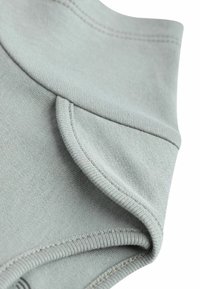 Tessuto grigio con una texture liscia, caratterizzato da un colletto drappeggiato e cuciture impeccabili. Il design include una leggera plissettatura sulla scollatura.