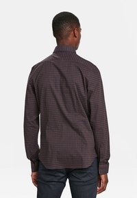 Hnědá kostkovaná košile na knoflíky s klasickým límcem a dlouhými rukávy, kterou charakterizuje hladká textilie a dobře padnoucí střih.