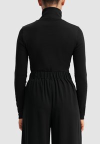 Crna dugaka majica s turtleneck ovratnikom i uskim krojem, izrađena od mekog materijala. Ima nabran pojas i glatku teksturu.