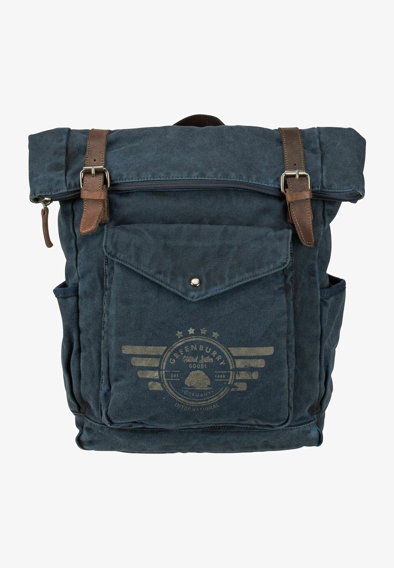 Sac à dos en toile bleu foncé avec des sangles en cuir marron. Il possède une poche frontale, une fermeture éclair sur le dessus et un logo avec des éléments décoratifs.