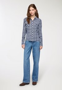 Camicia a maniche lunghe a quadri blu e bianchi con colletto button-down, due tasche sul petto, abbinata a jeans a gamba larga blu chiaro e stivali marroni.