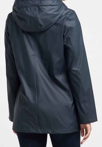 Veste imperméable bleu marine avec capuche, présentant une texture lisse, des manches longues et un ourlet légèrement incurvé. Les poignets ajustables et les coutures sont visibles.