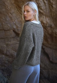 Szary, teksturowany sweter dziany o luźnym kroju, noszony na białej koszuli. W połączeniu z jasnoszarymi spodniami dresowymi. Naturalne tło skalne.