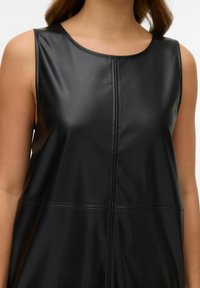 Robe noire sans manches en simili cuir lisse et brillant, avec un col rond et des coutures verticales décoratives sur le devant.