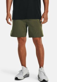 Olivgröna shorts i lättviktsmaterial, med sidofickor och en enkel design. Bärs med vita sportskor.