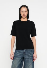 Μαύρη πλεκτή μπλούζα με κοντά μανίκια και στρογγυλή λαιμόκοψη, με απαλή υφή και άνετη εφαρμογή, συνδυασμένη με μπλε τζιν παντελόνι φαρδιάς γραμμής.