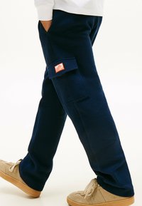 Marineblauwe wafelkatoenen broeken met een zijzak en een oranje label. Zachte textuur en een ontspannen pasvorm, gecombineerd met beige sneakers.