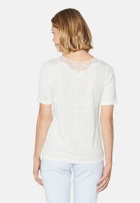 Weißes kurzärmliges T-Shirt mit einem dekorativen Spitzenbesatz am hinteren Halsausschnitt. Der Stoff ist leicht und leicht strukturiert.
