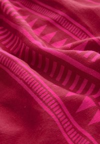 Tissu à motifs dans des nuances de fuchsia et de bordeaux, présentant des formes géométriques et des lignes. Texture lisse avec un léger éclat.