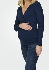 Blusa de maternidad de rayas azul oscuro con escote en V, manga larga y detalles texturizados, llevada sobre unos jeans oscuros, resaltando una barriga redondeada.