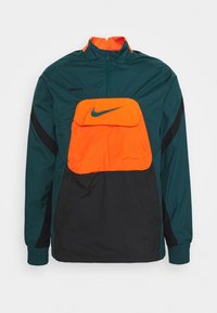 Chaqueta deportiva Nike de color verde oscuro, negro y naranja brillante con media cremallera y gran bolsillo delantero con el logo de la marca Nike.