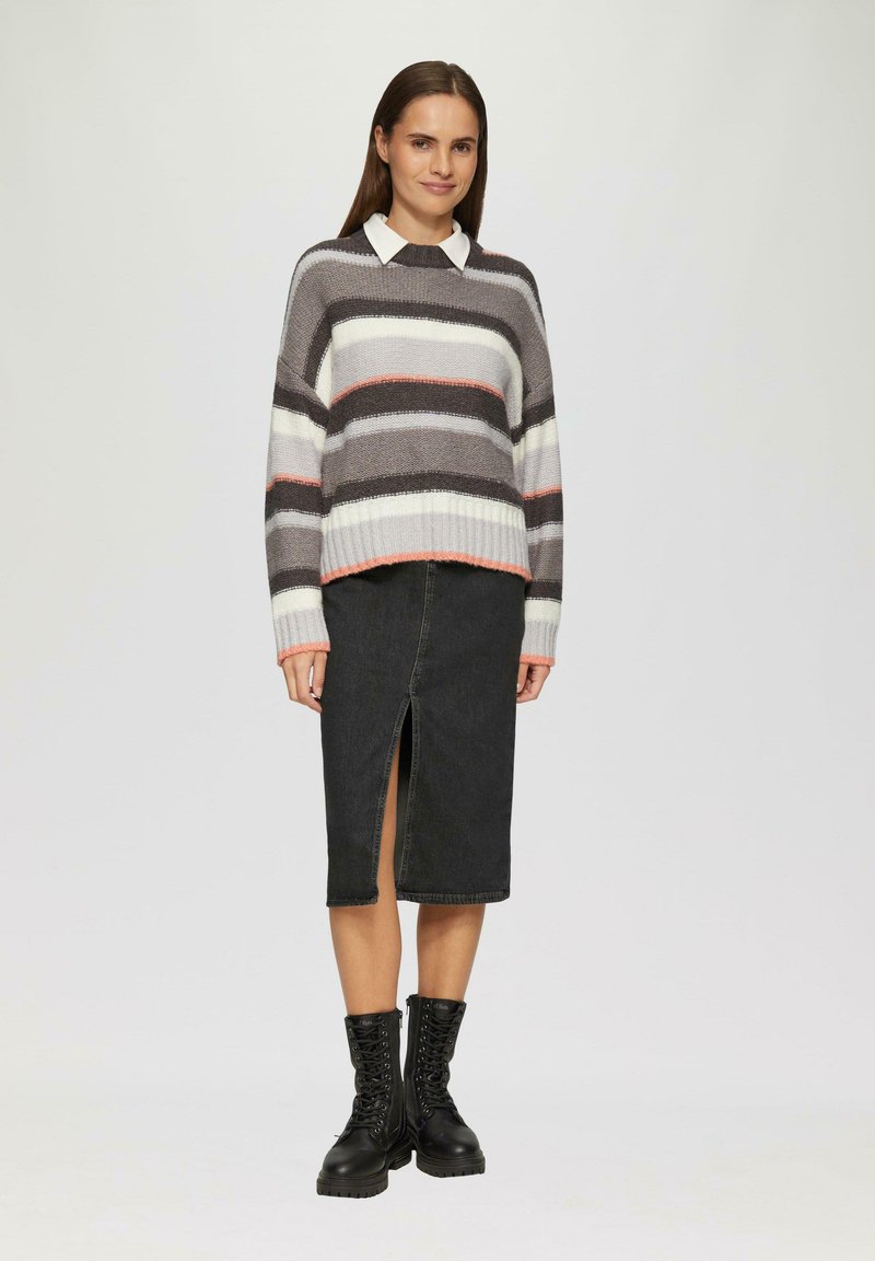 Pull rayé gris, blanc et rose ; col montant. Jupe en denim noir avec une fente sur le devant. Bottes de combat noires à lacets avec des semelles épaisses.