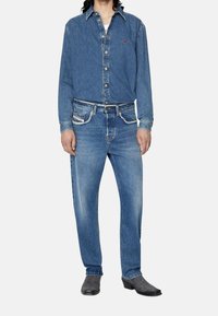 Camicia di jeans con collo a bottoni, maniche lunghe e logo sul petto; abbinata a jeans in denim chiaro con cuciture a contrasto e tasche.
