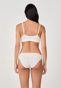 Bralette blanc en coton avec bretelles réglables, associé à un slip de bain à motif floral, de couleur claire, avec des détails à rayures verticales.