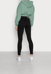 Zelená mikina s kapucí a elastickým pasem, spárovaná s černými skinny džíny s vysokým pasem a bílými platformovými teniskami.