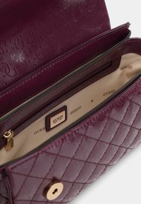 Borsa a tracolla viola trapuntata con finitura lucida, dotata di chiusura a bottone dorato e interno beige con rivestimento stampato con logo.