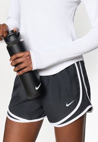 Mustad mustad spordilühikesed valgete aktsentidega, hoides musta veepudelit. Lühikesed püksid on valmistatud hingavast materjalist ja neil on Nike logo.