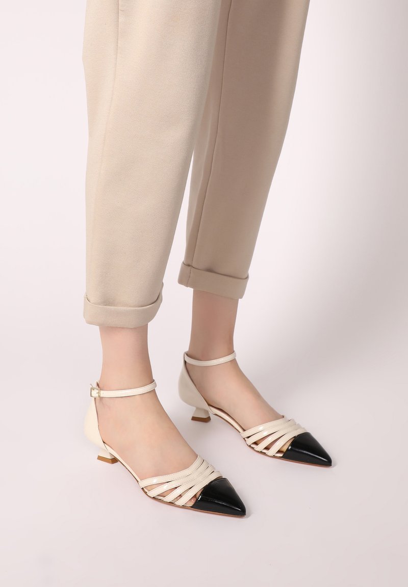 Beige Ballerinas mit Knöchelriemen und spitzem Zehenbereich mit schwarzem Einsatz, mehrfacher Riemen-Passform und kleinem Absatz. Glattleder-Oberfläche.